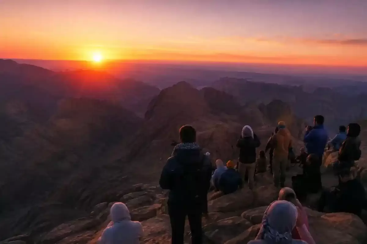 Hikers watching a golden sunrise over rugged mountain peaks from Mount Sinai summit